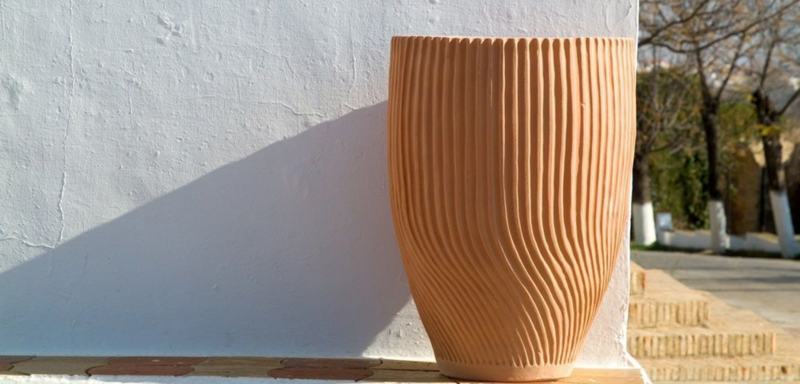 Ribbed terracotta planter placed against a white wall with a shadow cast on the wall.