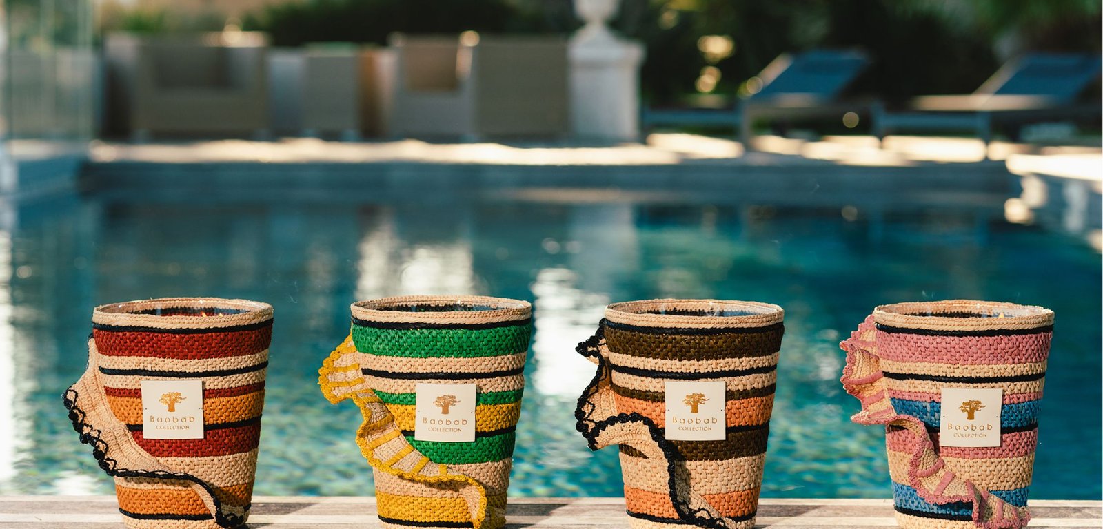 Four handcrafted Baobab Collection baskets in red, green, brown, and pink, placed in front of a swimming pool